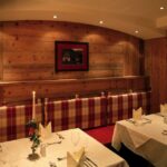 Ein gemütlicher Restaurantbereich mit Holzwänden, gepolsterten Sitzen, gedeckten Tischen mit weißen Tüchern, Kerzen und gerahmten Bildern an den Wänden.