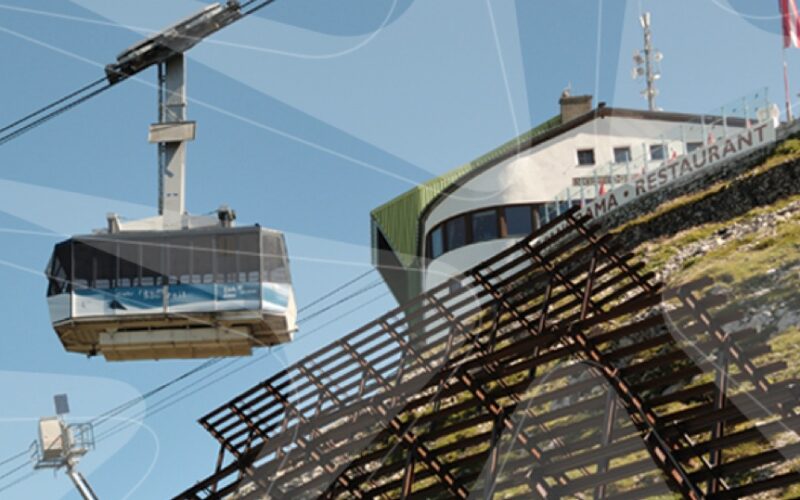 Eine Seilbahn fährt an einem klaren Tag zu einer Bergstation in der Nähe eines Gebäudes mit der Aufschrift "RESTAURANT".