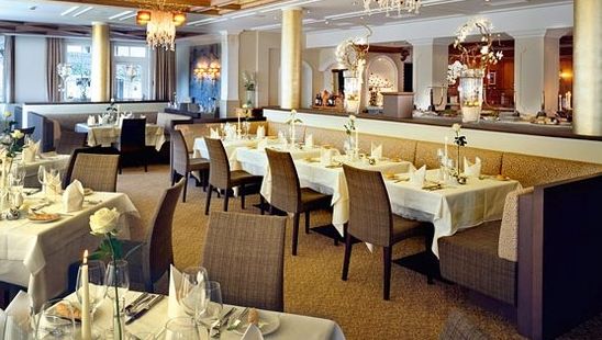 Ein geräumiger, eleganter Restaurantbereich mit ordentlich gedeckten Tischen, gepolsterten Stühlen, Kronleuchtern und dekorativer Beleuchtung.