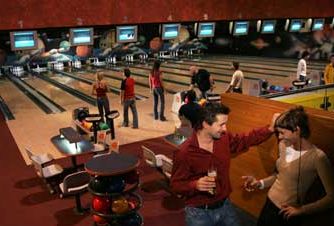 Auf einer Bowlingbahn mit mehreren Bahnen, bunten Bowlingkugeln und Fernsehbildschirmen über den Bahnen trifft man sich zum Bowling.