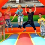 Fünf Kinder springen und spielen in einer bunten, aufblasbaren Hüpfburg.