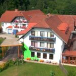 Luftaufnahme eines großen Gebäudekomplexes mit roten Ziegeldächern, Balkonen, Sitzgelegenheiten im Freien und umliegenden Grünflächen.