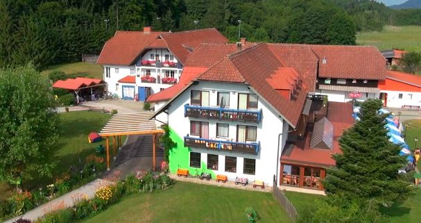 Luftaufnahme eines großen Gebäudekomplexes mit roten Ziegeldächern, Balkonen, Sitzgelegenheiten im Freien und umliegenden Grünflächen.