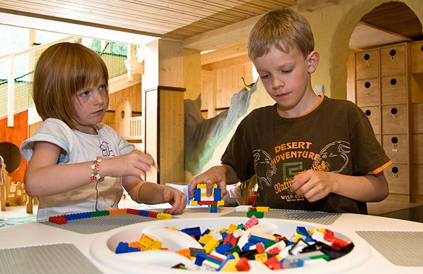 Zwei Kinder sitzen an einem Tisch und bauen mit bunten Plastikklötzen in einem Spielzimmer mit Holzmöbeln und einer gemütlichen Atmosphäre.