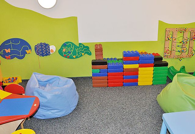 Ein Kinderspielzimmer mit bunten Schaumstoffblöcken, Sitzsäcken, an der Wand befestigtem Spielzeug und verspielten Wanddekorationen in Form von Fischen.