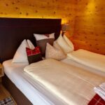 Ein ordentlich gemachtes Doppelbett mit mehreren Kissen und einer rot karierten Decke in einem holzgetäfelten Raum mit Wandlampen und einem Nachttisch.