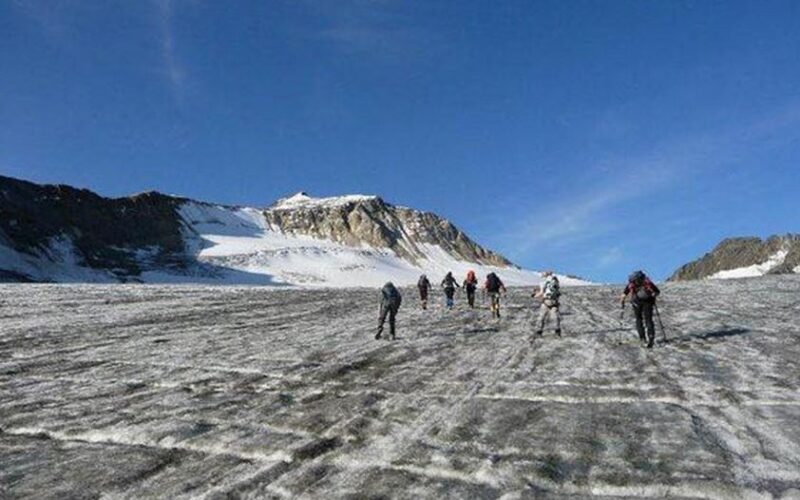 Eine Gruppe von Bergsteigern wandert über einen Gletscher zu einem schneebedeckten Berg unter einem strahlend blauen Himmel.