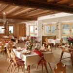 Ein gemütlicher Speisesaal mit Holzböden und -decken, gedeckten Tischen mit Blumen und großen Fenstern, die viel Tageslicht hereinlassen.