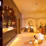 Eine Spa-Lounge mit Liegestühlen, gerollten Handtüchern, brennenden Kerzen, Wandkunst und gedämpfter Beleuchtung, die eine entspannende und einladende Atmosphäre schafft.