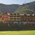 Ein mehrstöckiges Hotel mit Balkonen und einer roten Spiralrutsche vor einem bewaldeten Hügel im Sonnenlicht.