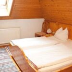 Ein kleines Zimmer im Dachgeschoss mit Holzwänden, zwei zusammengeschobenen Einzelbetten, einem Fernseher, einem Teppich, einem Heizkörper, einem Nachttisch und einer Lampe unter einer schrägen Decke mit einem Dachfenster.