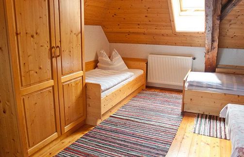 Holzgetäfeltes Schlafzimmer im Dachgeschoss mit zwei Einzelbetten, einem Holzschrank, gestreiften Teppichen, einem Heizkörper und einem Oberlichtfenster.