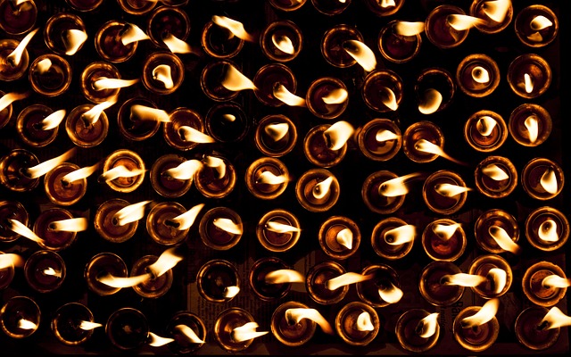 Reihen kleiner Kerzen, die mit sichtbaren Flammen brennen, von oben in einer schwach beleuchteten Umgebung betrachtet.