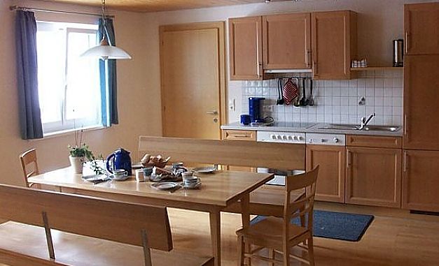 Eine Küche und ein Essbereich mit Holzschränken, einem Herd, einer Spüle und einem Holztisch, der mit Geschirr, Tassen und einer Teekanne für das Frühstück gedeckt ist.