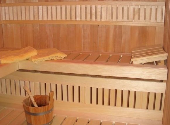 Hölzernes Interieur einer Sauna mit Bänken, einem Eimer und einer Schöpfkelle sowie gefalteten Handtüchern auf der oberen Bank.