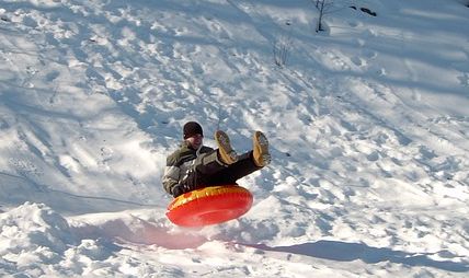 Eine Person in Winterkleidung gleitet auf einem roten aufblasbaren Schneeschlauch einen verschneiten Hügel hinunter.