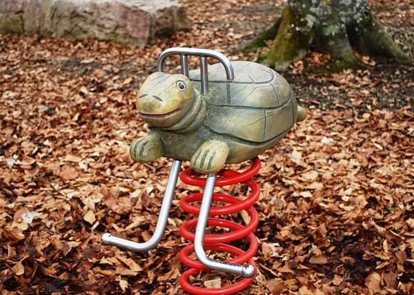 Ein schildkrötenförmiges Federspielzeug für den Spielplatz ist von gefallenen braunen Blättern umgeben.