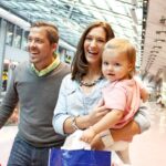 Ein Mann, eine Frau und ein kleines Kind mit Einkaufstaschen gehen gemeinsam durch ein hell erleuchtetes Einkaufszentrum.