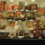 Eine Glasvitrine voller Vintage-Zaubertrick-Sets, Bücher, Karten und Box-Sets, die auf mehreren Regalen angeordnet sind.