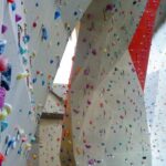 Indoor-Kletterhallenwände mit zahlreichen bunten Griffen und Routen auf hohen, abgewinkelten Flächen.