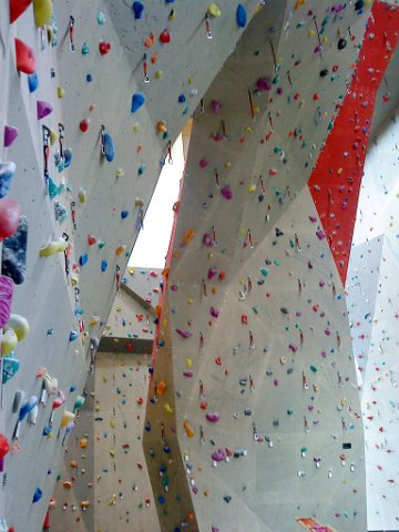 Indoor-Kletterhallenwände mit zahlreichen bunten Griffen und Routen auf hohen, abgewinkelten Flächen.