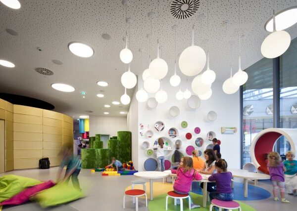 Kinder spielen und interagieren in einem hell erleuchteten, modernen Indoor-Spielzimmer mit farbenfrohen Möbeln, runden Leuchten und verspielten Wanddekorationen.