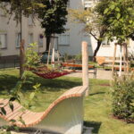 Ein kleiner Stadtpark mit einer modernen Holzbank, einer roten Hängematte, grünem Gras, Bäumen und nahe gelegenen Wohnhäusern.