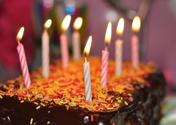 Ein Schokoladenkuchen mit gelben und orangefarbenen Streuseln wird von neun brennenden Geburtstagskerzen gekrönt.