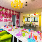 Ein farbenfroh dekorierter Raum für einen Kindergeburtstag mit bunt gedeckten Tischen, Partyhüten und einem "Happy Birthday"-Schild an der Wand.
