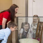 Eine Frau und drei kleine Kinder betrachten einen antiken Stuhl, der in einem Museum hinter Glas ausgestellt ist.