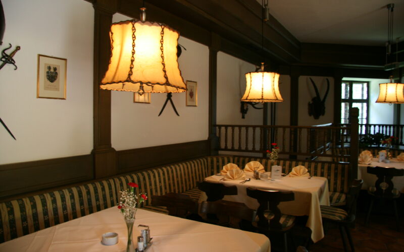 Ein gemütliches Restaurant mit gemusterten Bänken, weißen Tischtüchern, gefalteten Servietten, Blumenvasen und warmen Hängelampen an der Decke.