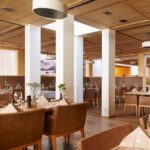 Moderner Essbereich in einem Restaurant mit braunen Lederstühlen, Holztischen mit Gläsern und Servietten, Holzdecke und weißen Säulen. Der Raum ist menschenleer.