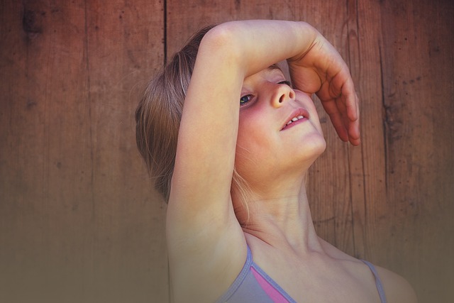 Ein junges Mädchen steht vor einer Holzwand mit erhobenem rechten Arm, der einen Teil ihrer Stirn und ihrer Augen bedeckt.