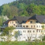 Ein großes, mehrstöckiges Gebäude mit einem dunklen Dach, umgeben von grünen Bäumen und Vegetation, an einem bewaldeten Hang.