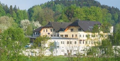 Ein großes, mehrstöckiges Gebäude mit einem dunklen Dach, umgeben von grünen Bäumen und Vegetation, an einem bewaldeten Hang.