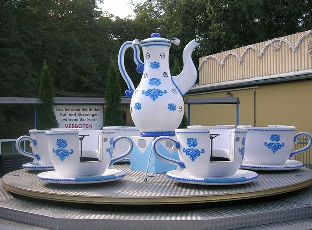 Ein sich drehendes Vergnügungspark-Fahrgeschäft als Teeservice mit großen Teetassen und einer Teekanne mit blauen Blumenmustern auf einer Metallplattform.
