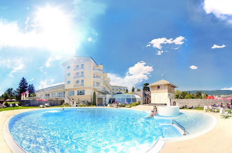 Ein heller, sonniger Tag an einem Hotel-Freibad mit klarem, blauem Wasser, einer schwimmenden Person und dem Hotelgebäude im Hintergrund.