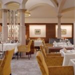 Elegantes Restaurantinterieur mit gewölbten Decken, gelb gepolsterten Stühlen, weißen Tischdecken, gedeckten Tischen und gerahmten Kunstwerken an den Wänden.