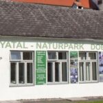 Ein weißes Gebäude mit der Aufschrift "Thayatal-Naturpark Dobersberg" mit Schildern für ein Infozentrum und einen Museumsshop sowie mehreren Fenstern und Plakaten an der Wand.