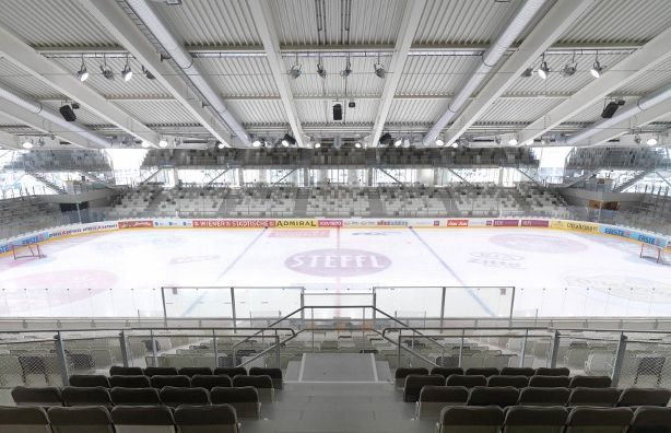 Leere Eishockeyhalle mit sichtbaren Sitzplätzen, übersichtlichen Banden und Werbung auf der Eisfläche und an den Wänden.