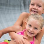 Zwei kleine Kinder lächeln und umarmen sich, während sie eine Wasserrutsche hinunterfahren.