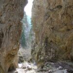 Enge, felsige Schlucht mit steilen Klippen auf beiden Seiten, etwas Grün in der Ferne und einem felsigen Bachbett am Fuße.