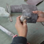 Eine Person glättet mit Schleifpapier eine kleine Steinskulptur auf einem Arbeitstisch mit Feilen und anderen Werkzeugen.