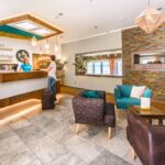 Ein Gast meldet sich an der Rezeption einer modernen Hotellobby mit Sitzecke, Steinakzenten und warmer Beleuchtung.