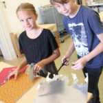 Zwei Kinder stehen an einem Tisch und schneiden mit einer Schere Dekorationspapier und Silberfolie aus, um im Haus zu basteln.