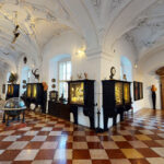 Verschnörkelter Museumssaal mit gewölbter, verzierter Decke, kariertem Boden, Vitrinen und antiken Globen und Artefakten an den Wänden.