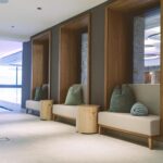 Drei eingebaute Sitzecken mit Holzrahmen, neutralen Kissen und Polsterungen säumen einen Flur mit hellem Bodenbelag und modernem Dekor.