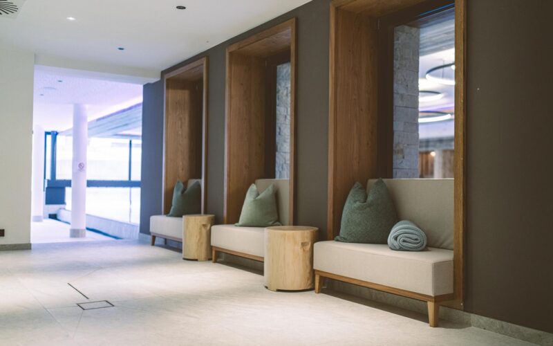 Drei eingebaute Sitzecken mit Holzrahmen, neutralen Kissen und Polsterungen säumen einen Flur mit hellem Bodenbelag und modernem Dekor.