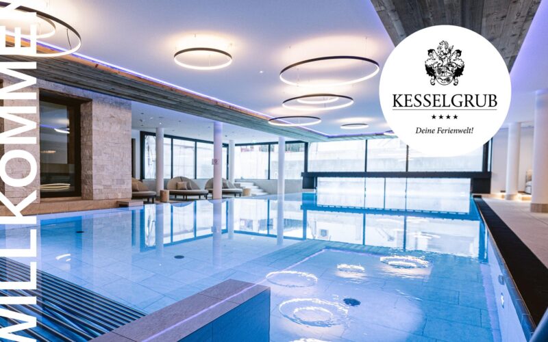 Hallenbadbereich mit moderner Beleuchtung, Liegestühlen und großen Fenstern; das Logo des Hotels Kesselgrub" und der Text WILLKOMMEN" sind auf dem Bild zu sehen.