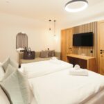 Modernes Hotelzimmer mit zwei sauber gemachten Einzelbetten, einem Sofa, einem an der Wand montierten Fernseher, Holzmöbeln und gedämpfter Umgebungsbeleuchtung.